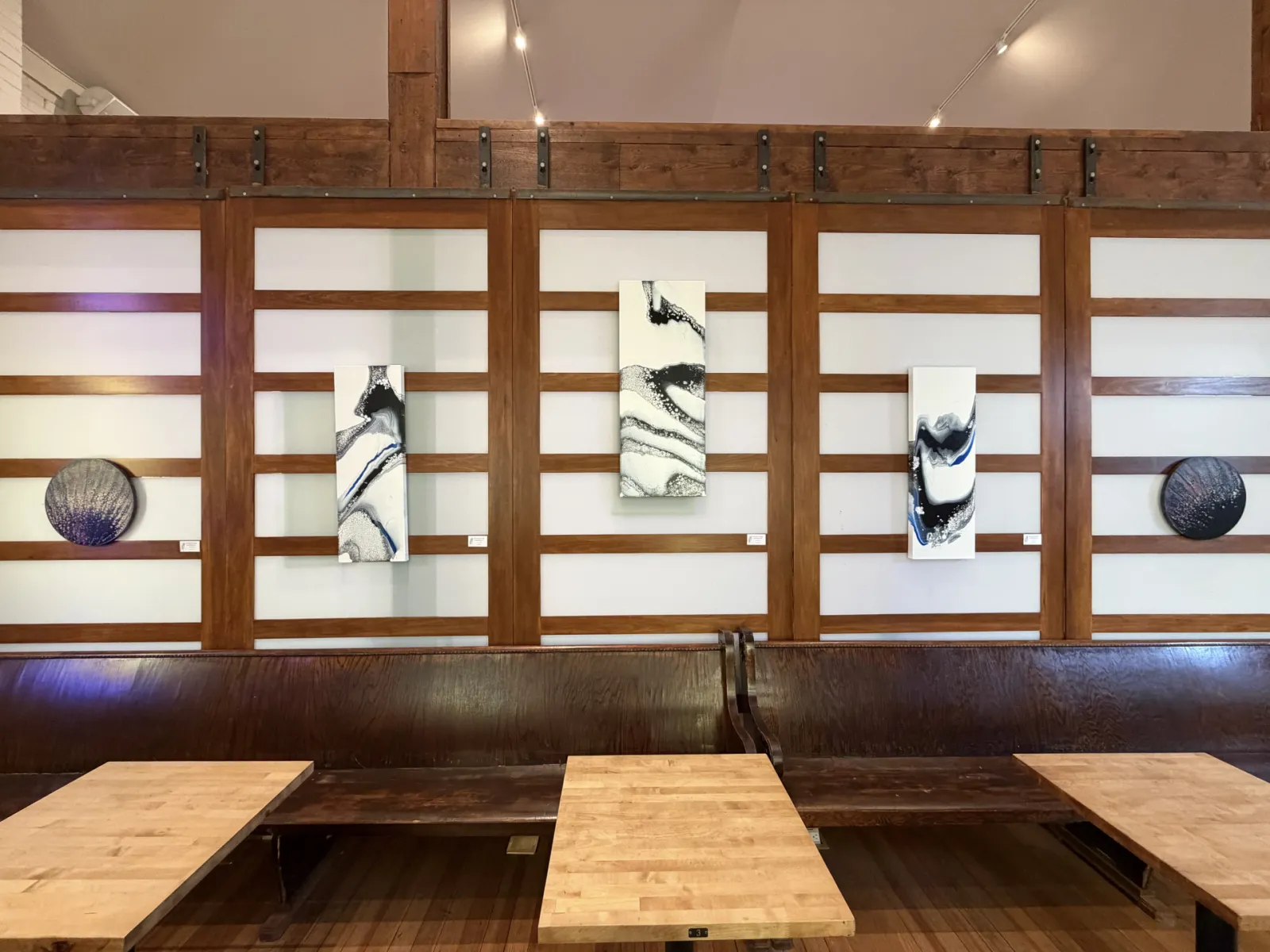 Abstract paintings hang on the wood-and-glass partition wall of the hall, with benches and small wooden tables arranged below
