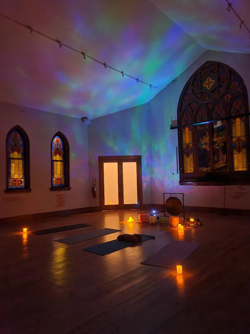 Candlelit sound bath setup with a gong, singing bowls, and mats beneath an aurora projection on the vaulted ceiling