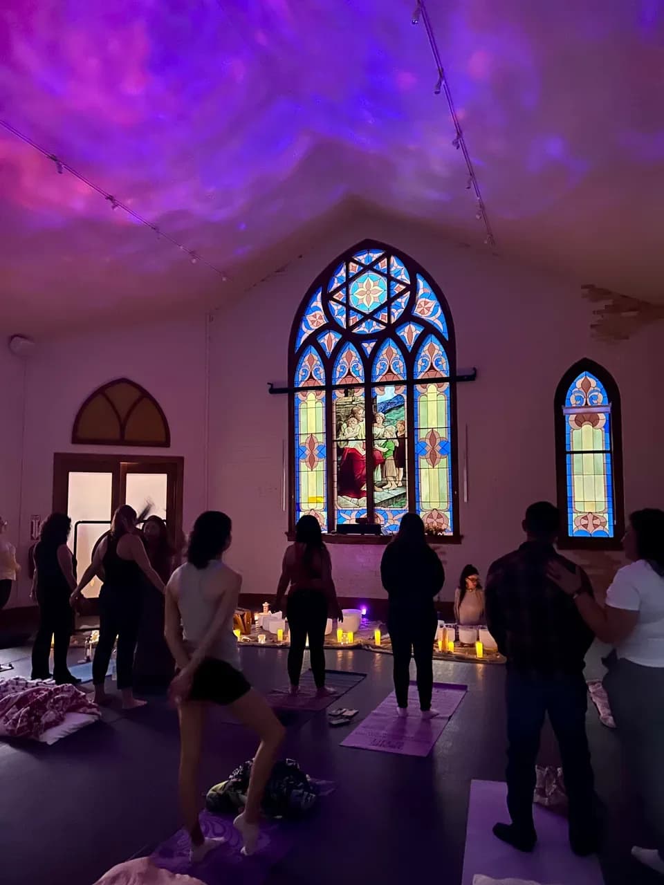 Participants gather among mats and candles under a projected purple sky during a sound bath event