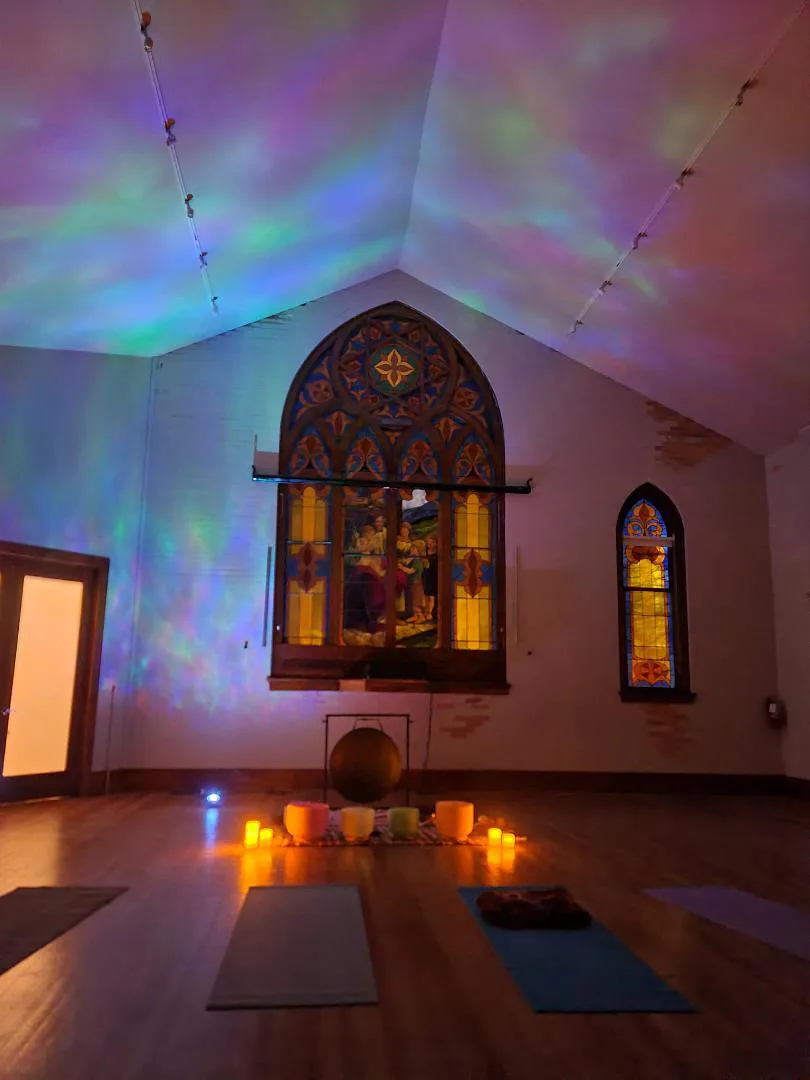 Singing bowls and candles glow beneath the stained-glass rose window during an evening sound bath