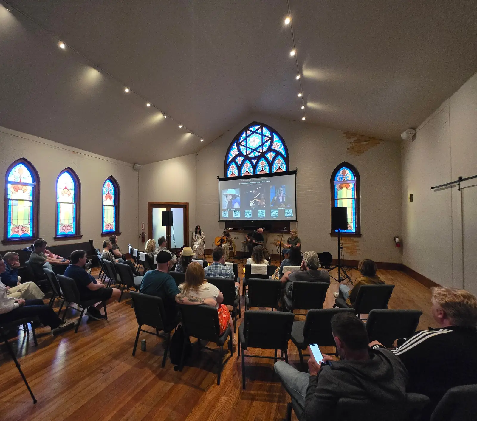 An audience watches an acoustic performance beneath the stained-glass rose window of the historic hall