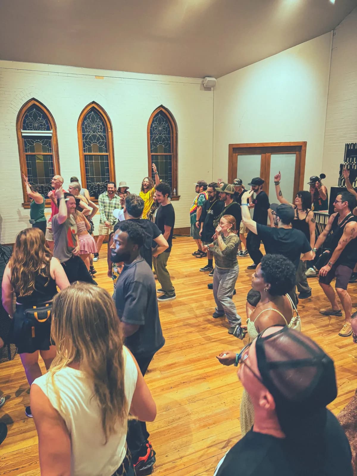 A crowd dances on the wood floor of the historic hall beneath its arched windows during an evening event