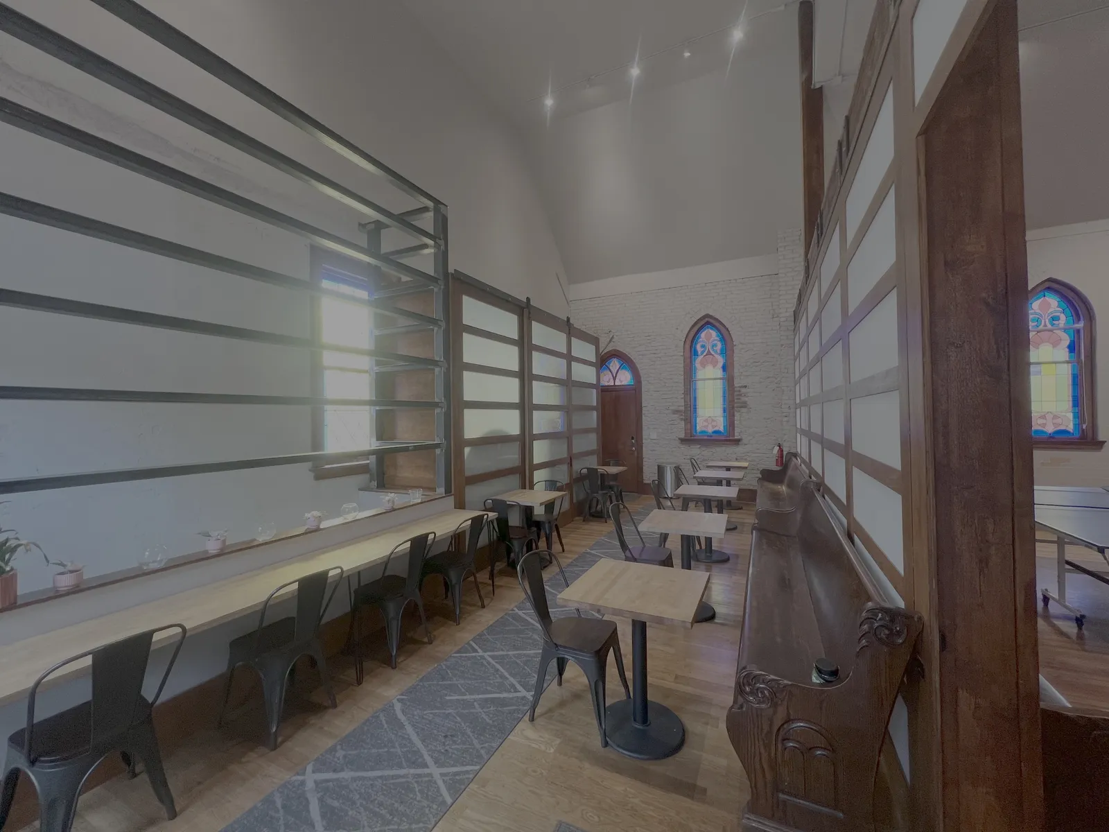 The lounge area with cafe tables, counter seating, and a carved wooden pew beneath stained-glass windows