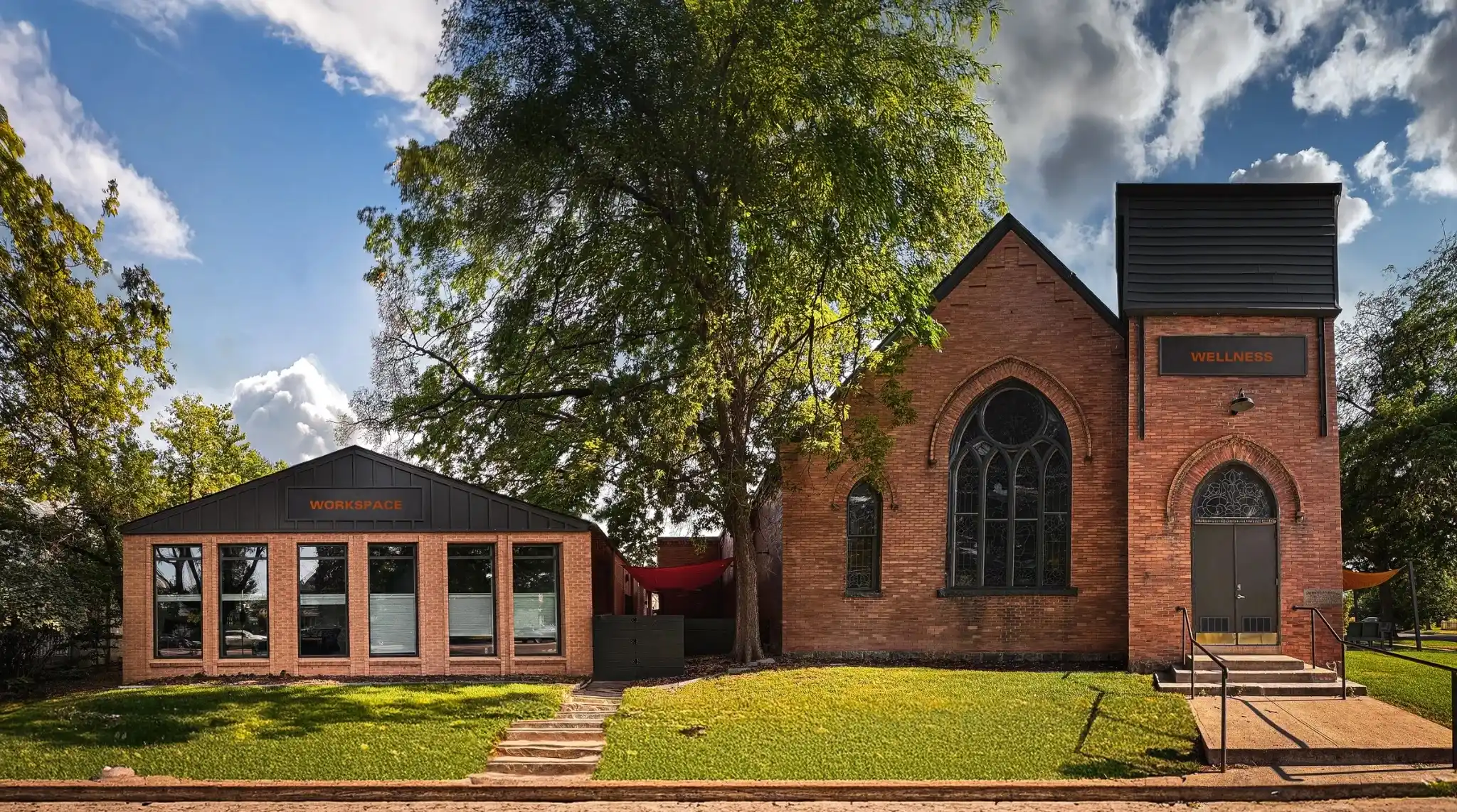 Front view of the restored 1905 brick building and its adjoining workspace under a dramatic sky