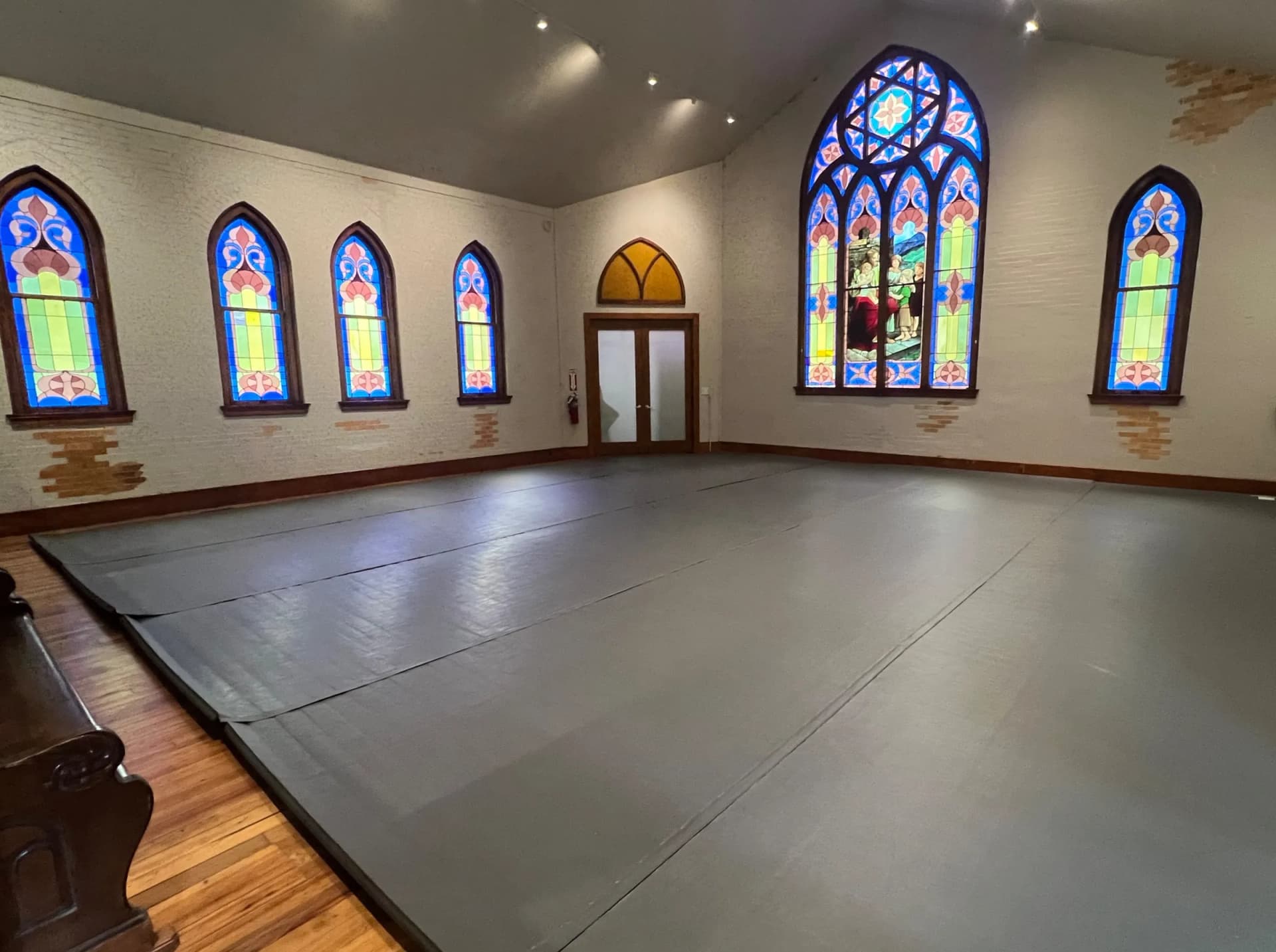 The hall's single full-coverage roll-out floor mat spans the room wall to wall beneath arched stained-glass windows