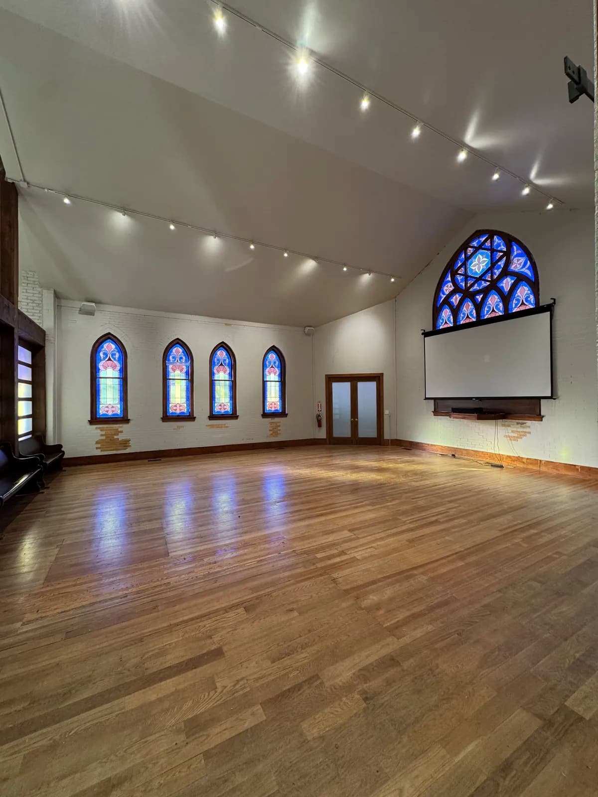 The empty hall with polished wood floors, arched stained-glass windows, and a projection screen beneath the rose window