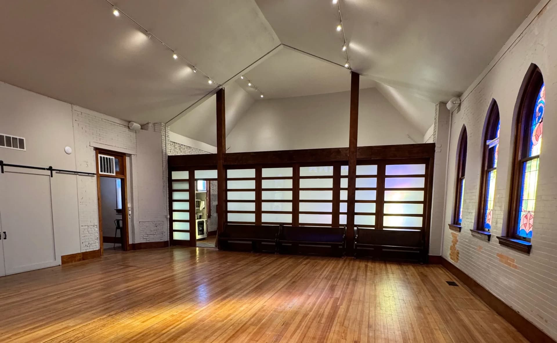 Sunlight warms the wood floor of the vaulted main hall, looking toward the shoji-screen partition and antique pews
