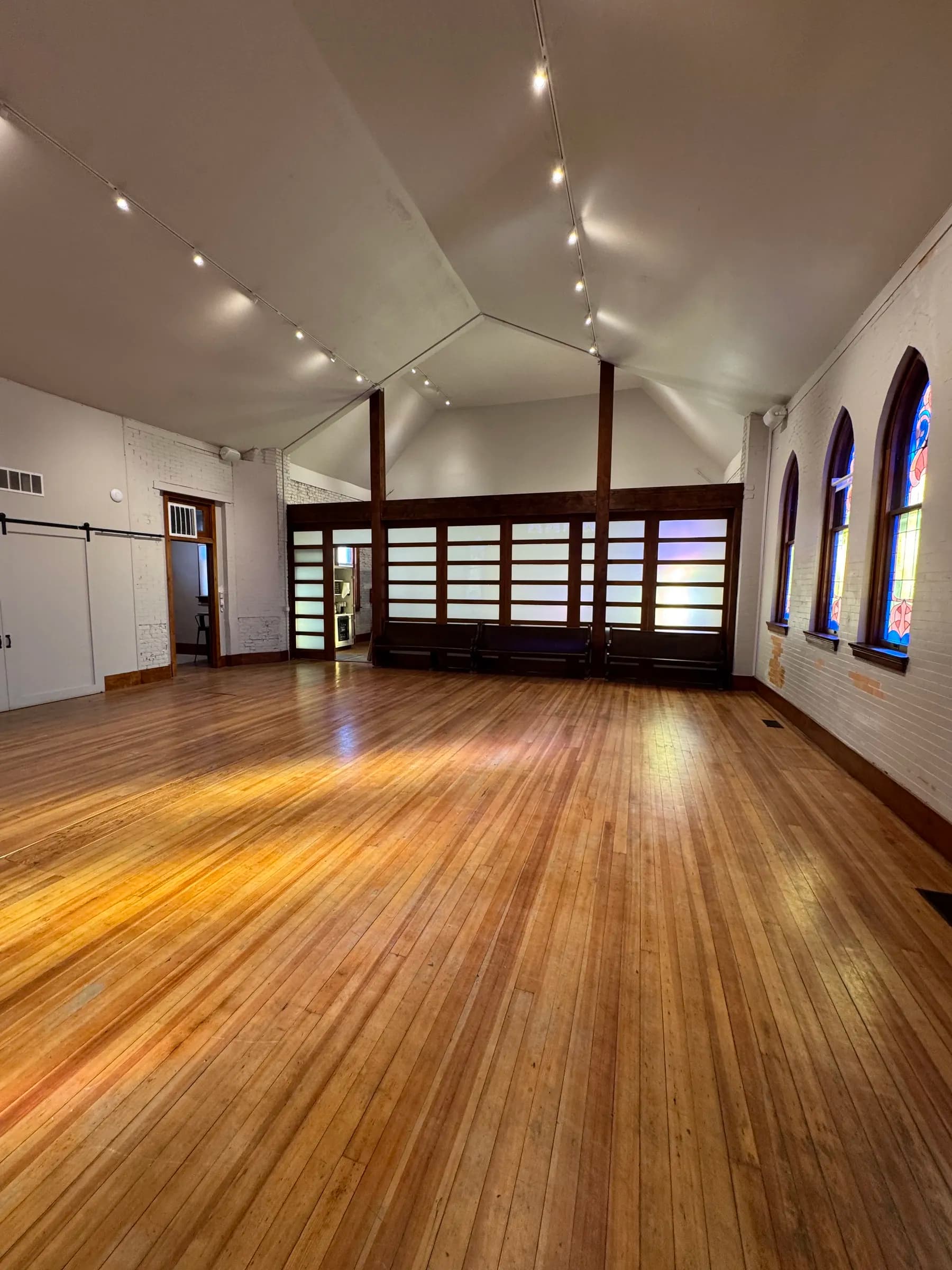 Sunlight warms the wood floor of the vaulted main hall, looking toward the shoji-screen partition and antique pews