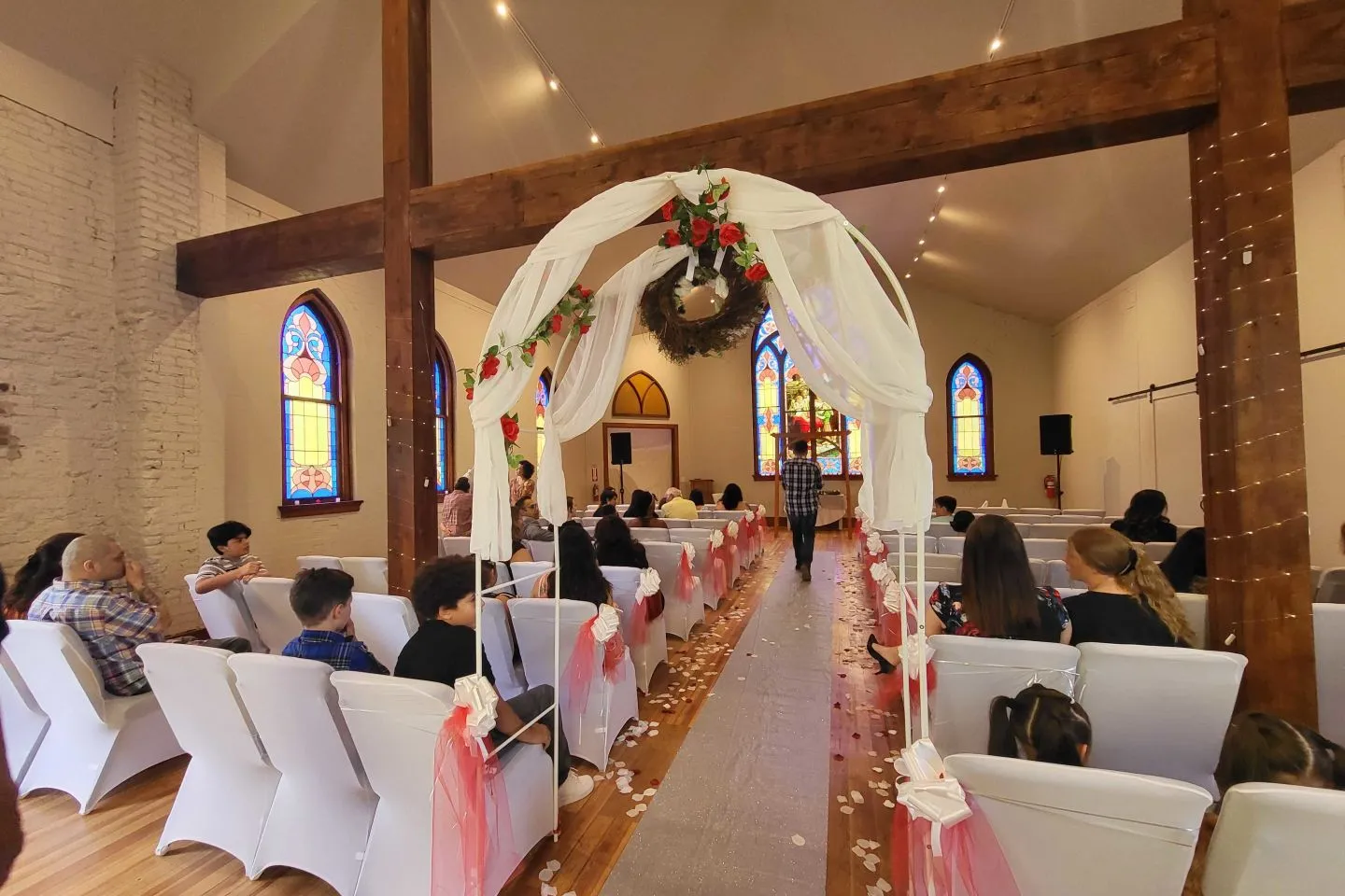 Guests seated for a wedding ceremony beneath the timber beams, looking down the aisle through a draped floral arch